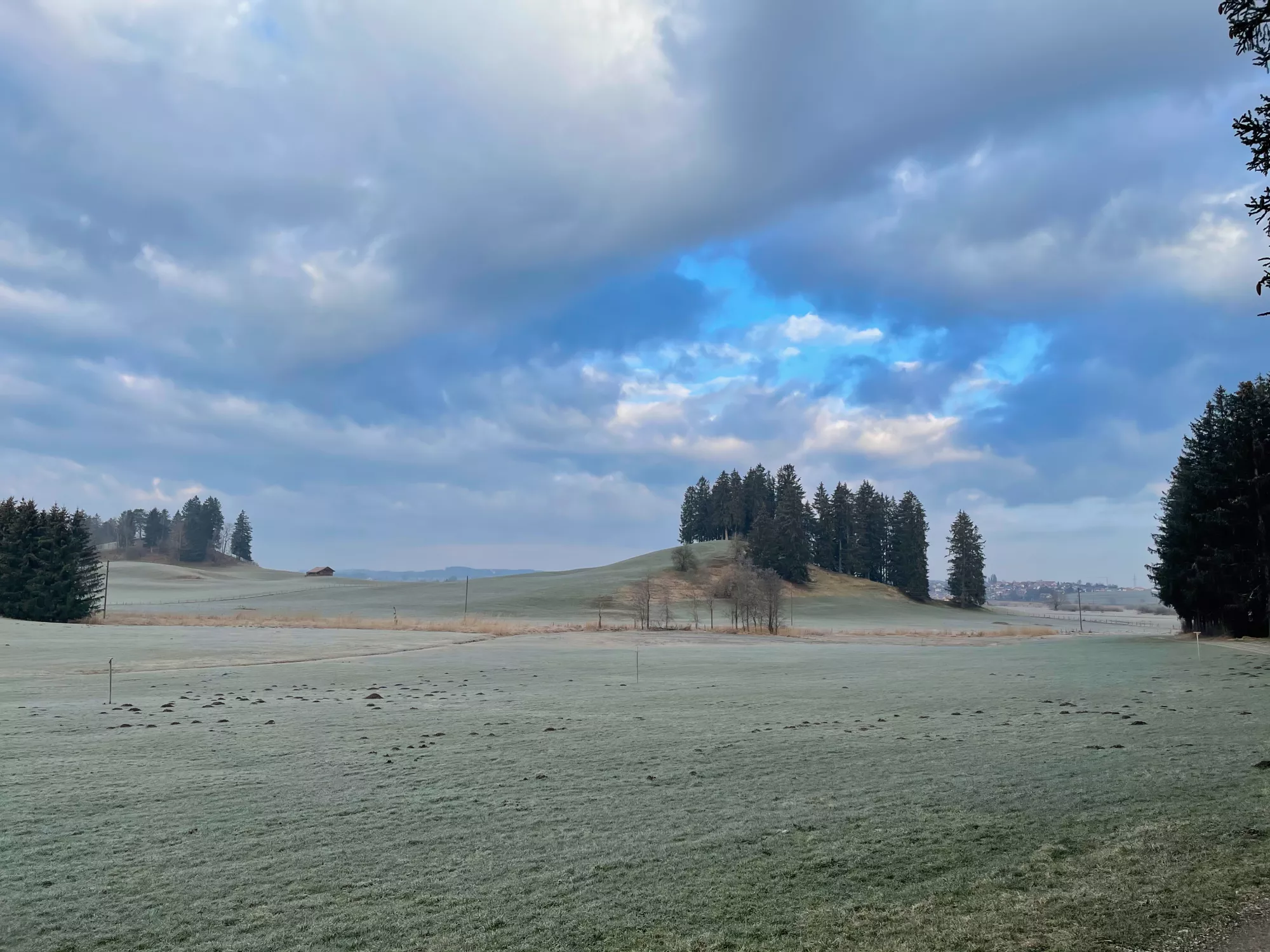 Sanfte Hügel und offene Felder rund um Aitrang im wechselnden Licht des Tages.