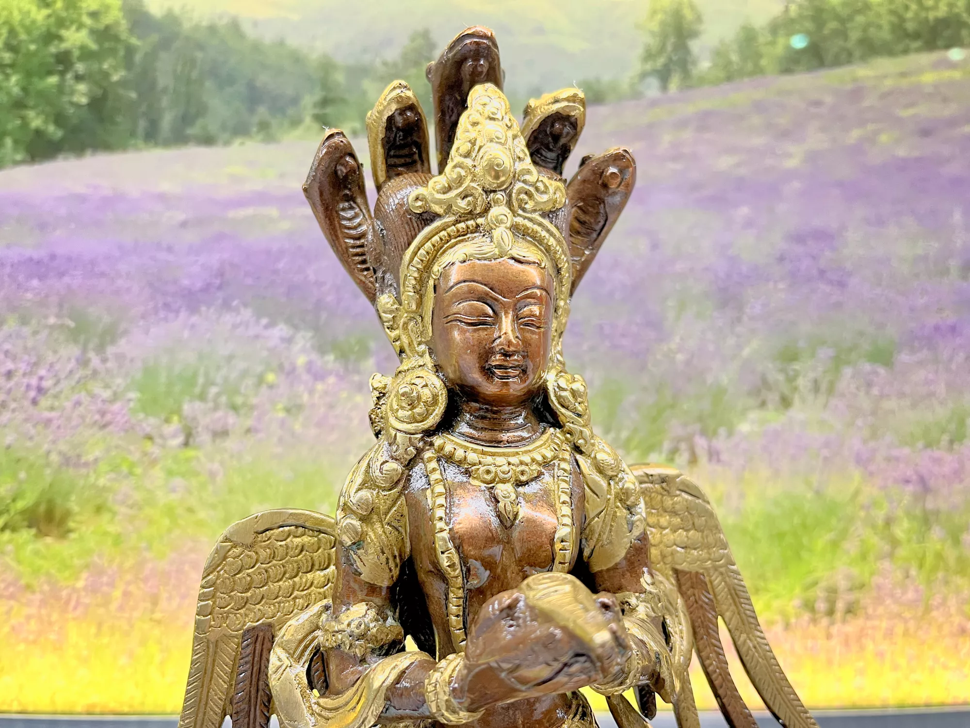 Detailreiche goldene Naga‑Statue mit mehreren Köpfen und filigranen Verzierungen vor einem Hintergrund mit Lavendelfeld und Hügeln.
