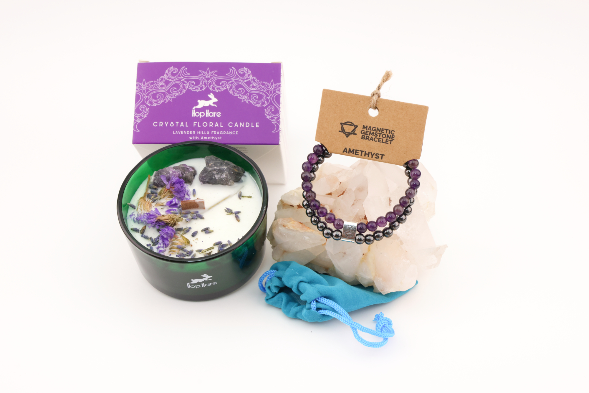 Grüne Hop‑Hare Duftkerze mit Citrin‑ und Amethyst‑Steinen sowie Blüten, daneben die lilafarbene Produktbox; rechts ein Amethyst‑Magnetarmband auf brauner Karte, präsentiert auf Bergkristallen mit türkisfarbenem Beutel.