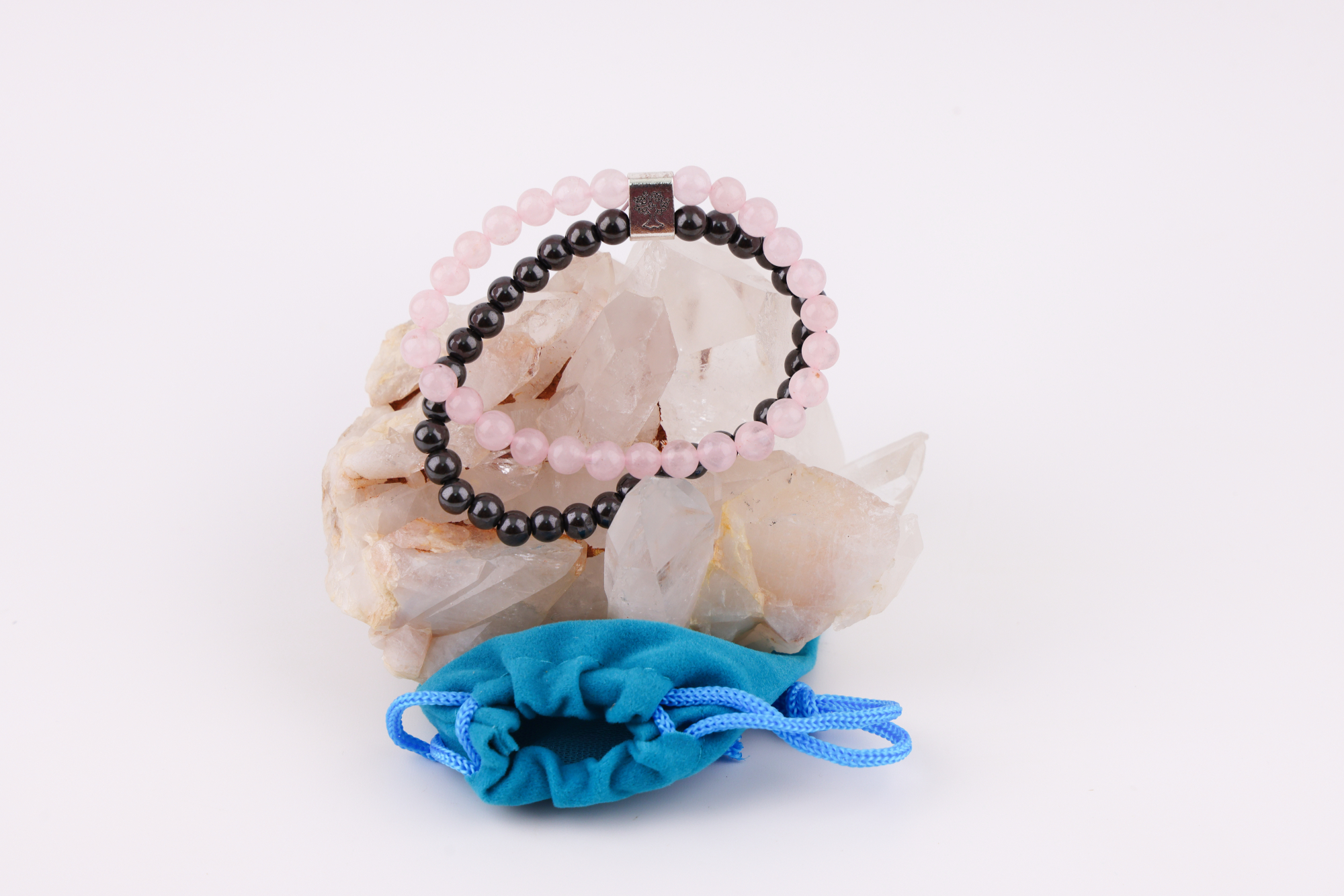Rosenquarz‑Magnetarmband auf Rosenquarz‑Kristall mit blauem Schmuckbeutel.