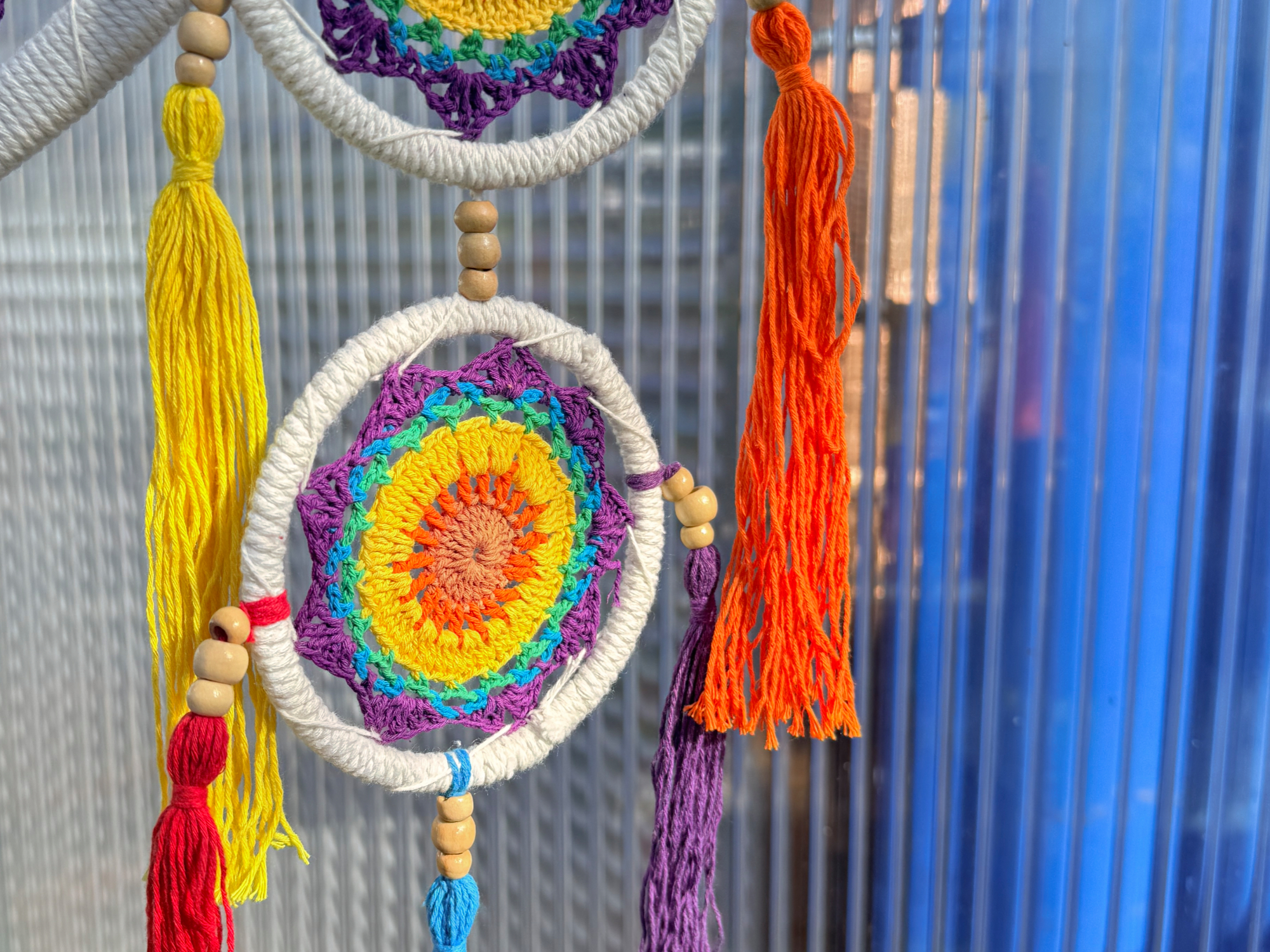 Nahaufnahme eines farbenfrohen, gehäkelten Traumfängers mit konzentrischen Regenbogenringen und kleineren, passenden Hängeelementen im Hintergrund.