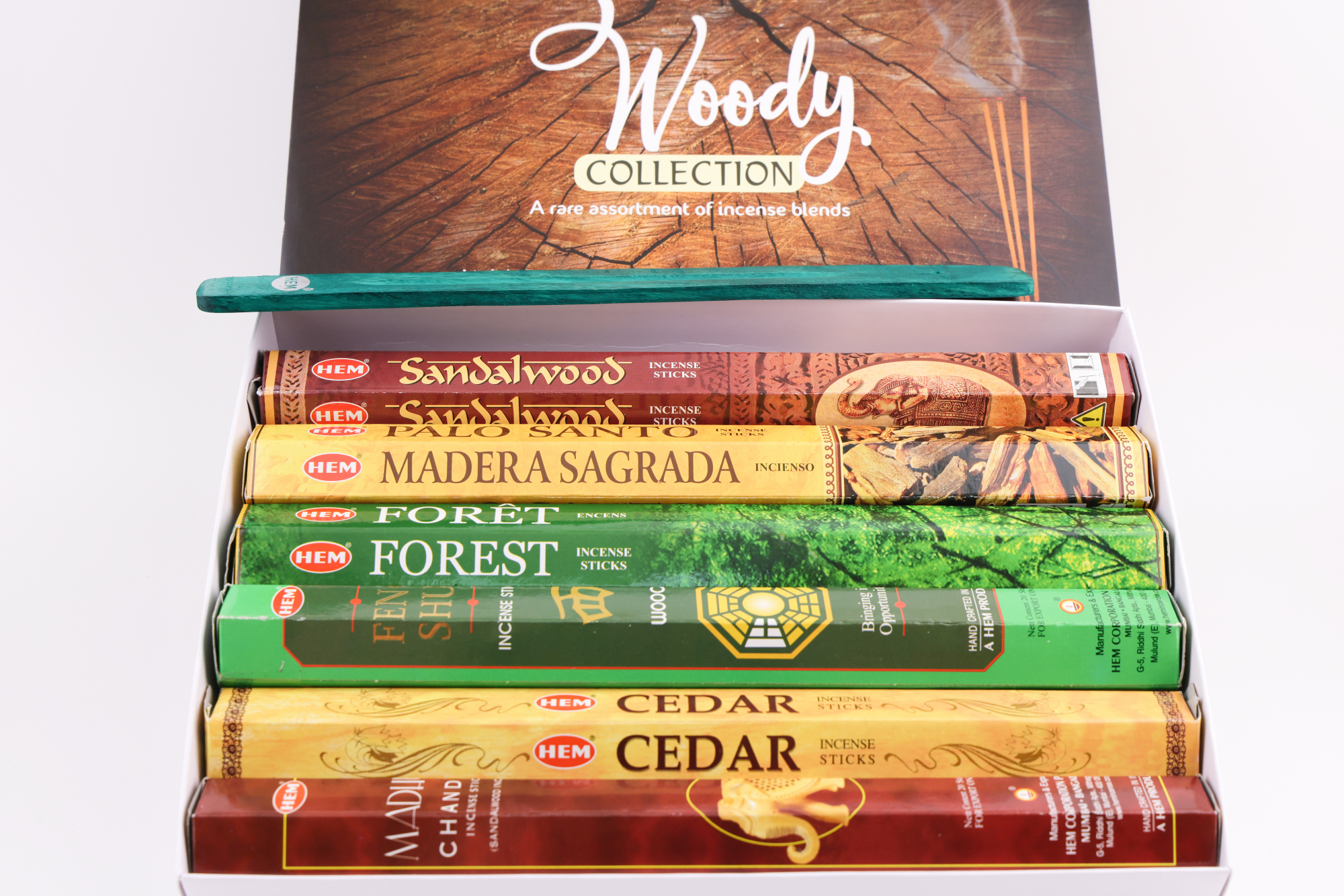 HEM Räucherwerk‑Set der Woody Collection mit verschiedenen Duftstäbchen‑Packungen (Cedar, Palo Santo, Foret, Feng Shui, Sandal), gelben Räucherstäbchen und grünem Halter.