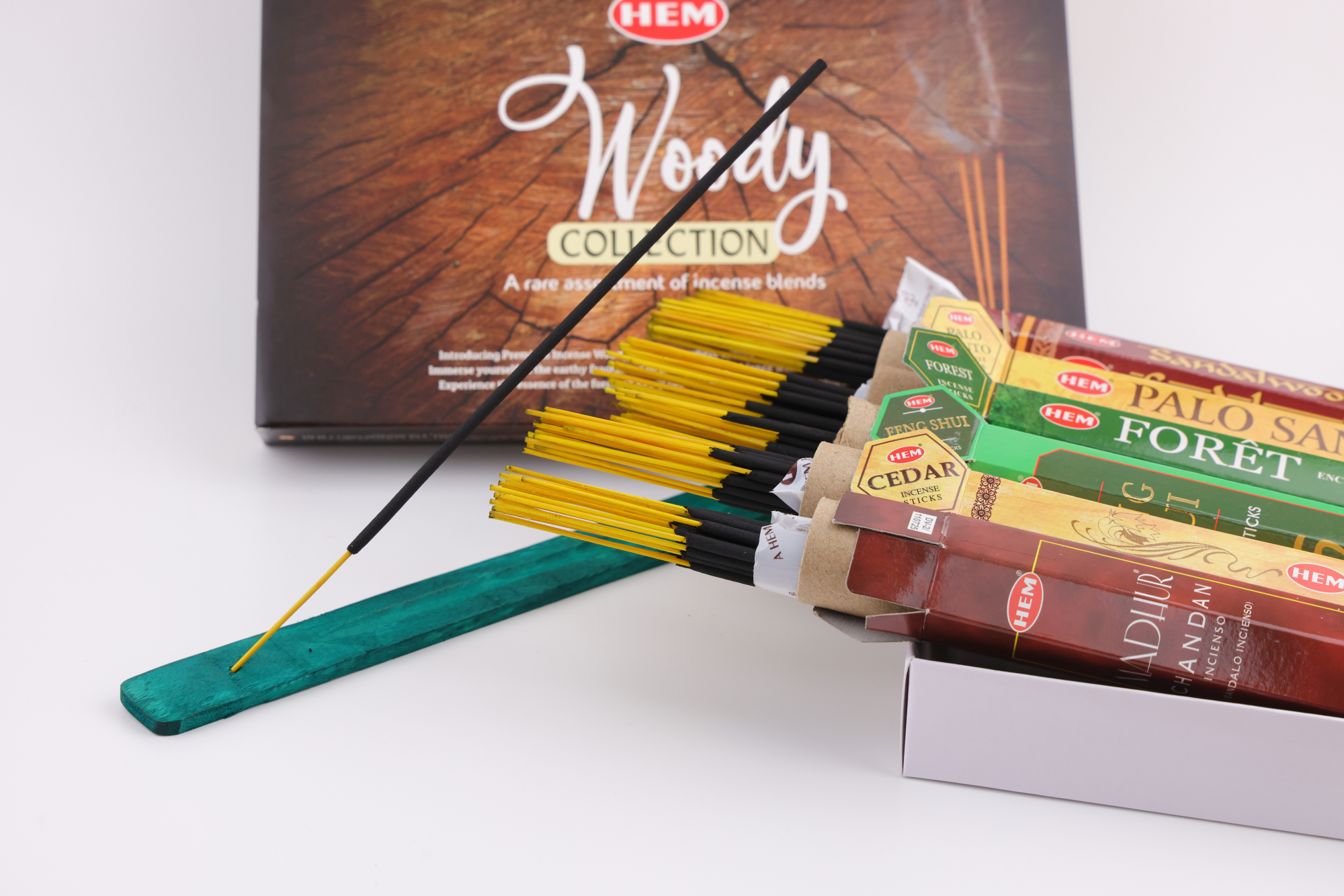 HEM Räucherwerk‑Set der Woody Collection mit verschiedenen Duftstäbchen‑Packungen (Cedar, Palo Santo, Foret, Feng Shui, Sandal), gelben Räucherstäbchen und grünem Halter.
