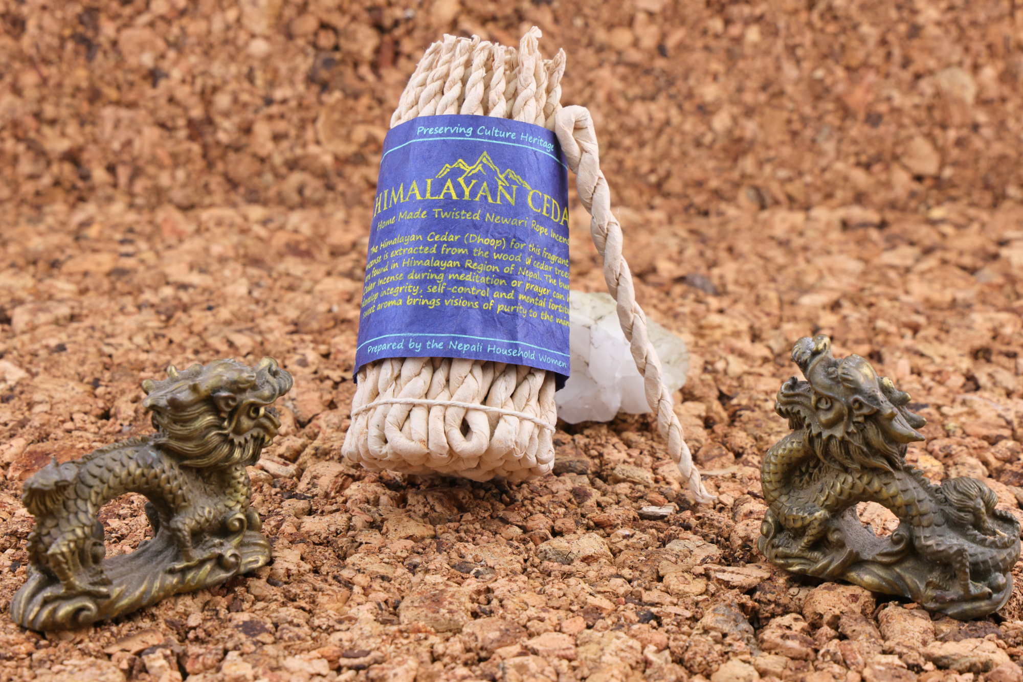 Handgedrehtes Himalaya‑Zeder‑Weihrauchseil mit blauem Etikett, dekoriert mit zwei bronzefarbenen Drachenfiguren und weißen Kristallen auf einer Korkunterlage.