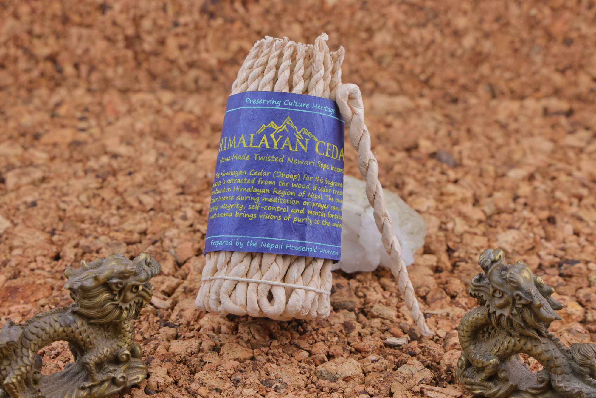 Handgedrehtes Himalaya‑Zeder‑Weihrauchseil mit blauem Etikett, dekoriert mit zwei bronzefarbenen Drachenfiguren und weißen Kristallen auf einer Korkunterlage.