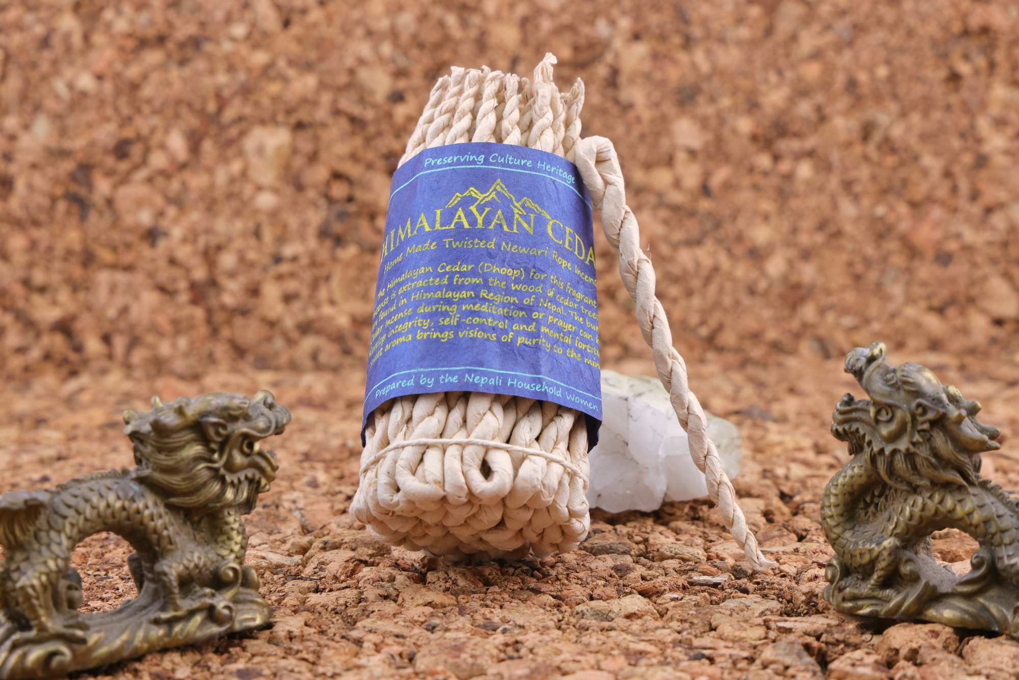 Handgedrehtes Himalaya‑Zeder‑Weihrauchseil mit blauem Etikett, dekoriert mit zwei bronzefarbenen Drachenfiguren und weißen Kristallen auf einer Korkunterlage.